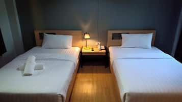 Una habitación de hotel con dos camas individuales, cada una con cabecera de madera, una mesita de noche con lámpara y una toalla enrollada sobre la cama.