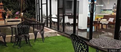 Un patio al aire libre con mesa y sillas, un pequeño jardín y vistas al cuarto contiguo.