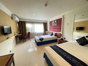 Habitación de hotel con dos camas, un escritorio, una silla, un televisor y una ventana con cortinas.