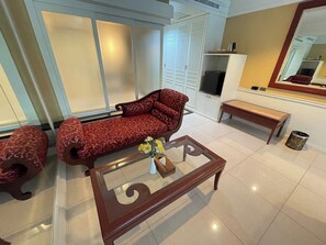 Una sala de estar con un sofá, una mesa de centro de vidrio, un banco y un televisor.