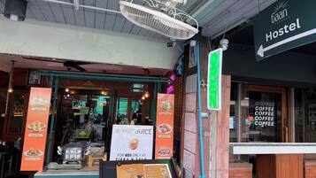 Entrada a un hostal con un cartel que indica que está abierto, un ventilador sobre la entrada y una pizarra publicitaria que ofrece jugo de coco.
