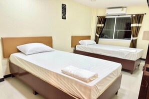 Habitación de hotel con dos camas, una ventana con cortinas, un equipo de aire acondicionado y una lámpara fijada a la pared.