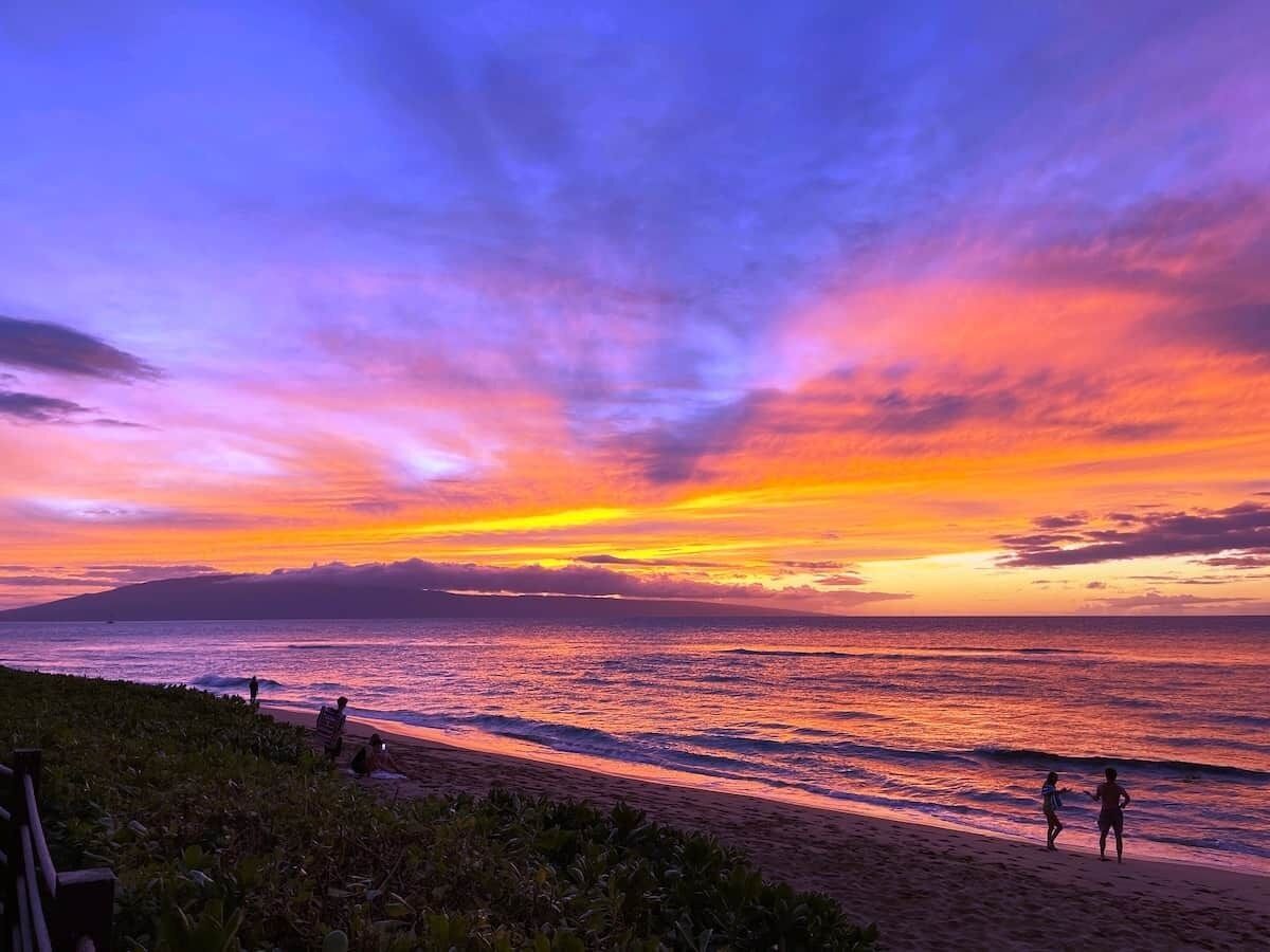 A beach with people, a sunset, and a clear sky.