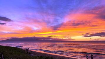 A beach with people, a sunset, and a clear sky.