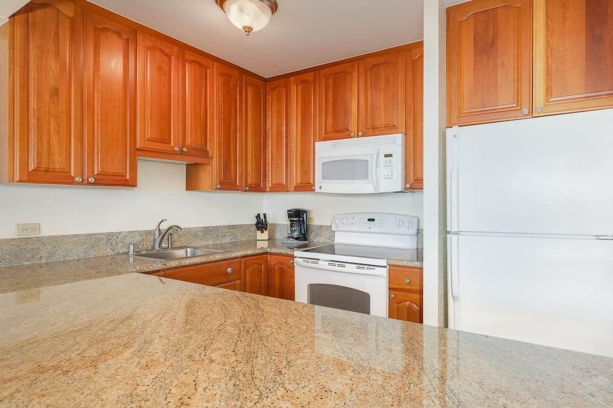 Une cuisine avec des meubles de rangement en bois, un micro-ondes blanc, une cuisinière et un réfrigérateur.
