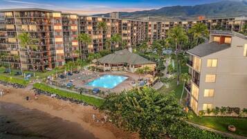 A hotel with multiple floors, a swimming pool, and palm trees.