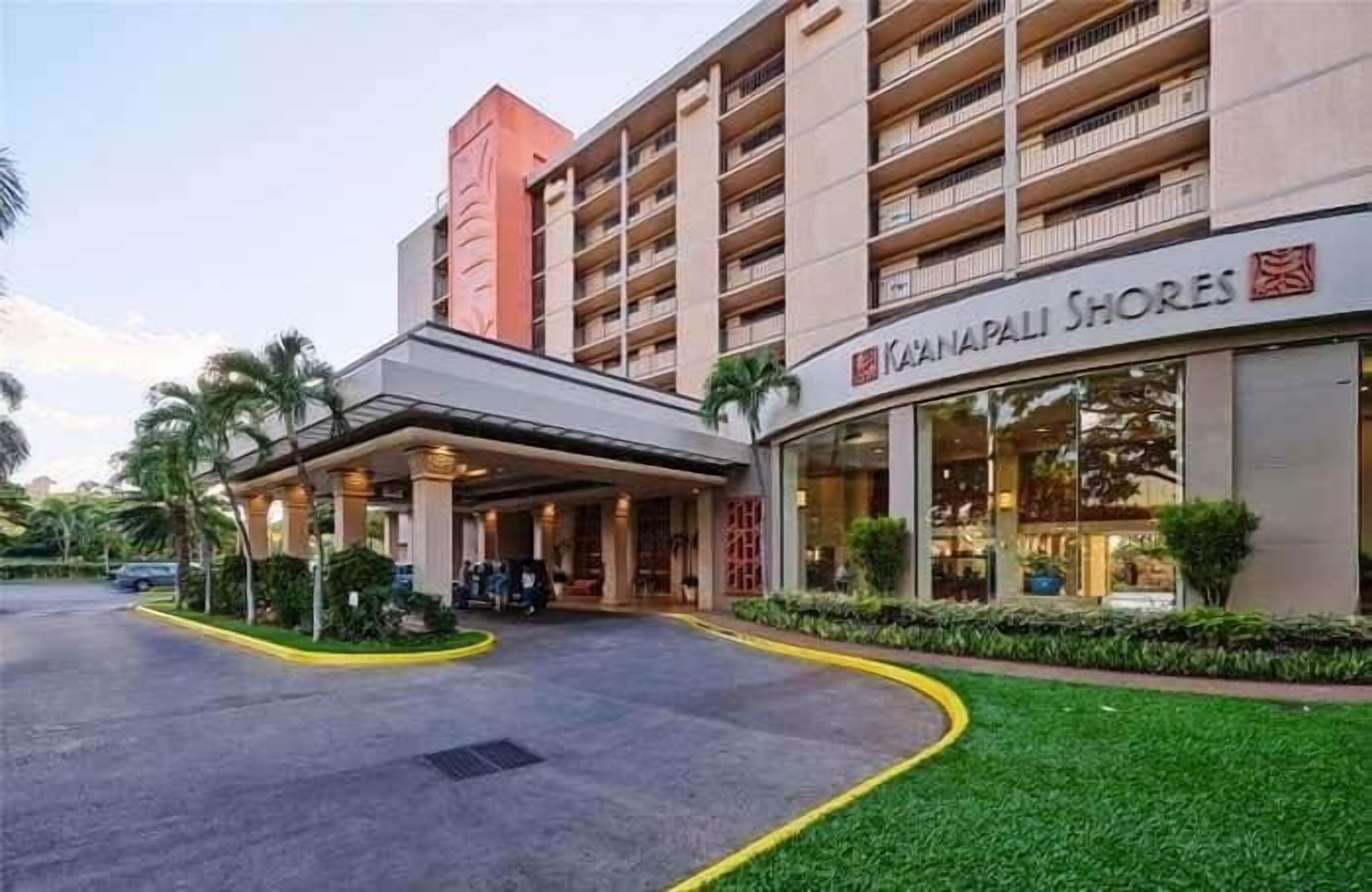 Et hotel med overdækket indgang, butiksvindue og parkeringsplads.