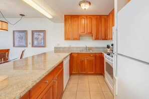 Eine Küche mit Holzschränken, einer Granit-Arbeitsplatte und einem weißen Kühlschrank.