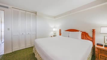 A hotel room with a large bed, a wardrobe, a bedside table with a lamp, and a nightstand with a clock.