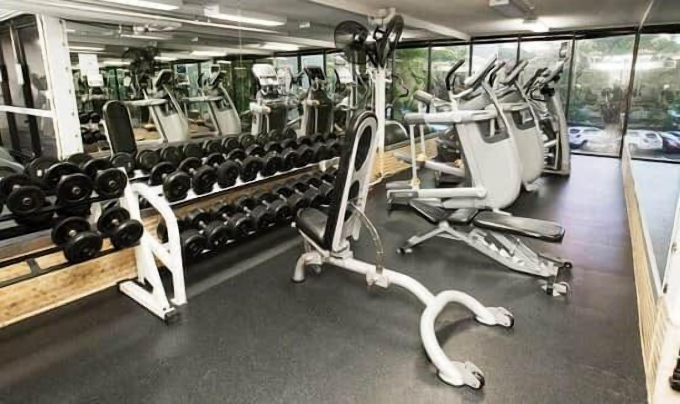 Et fitnessrum med træningsudstyr, herunder håndvægte, bænk og konditionsmaskiner.