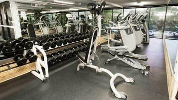 Et fitnessrum med træningsudstyr, herunder håndvægte, bænk og konditionsmaskiner.