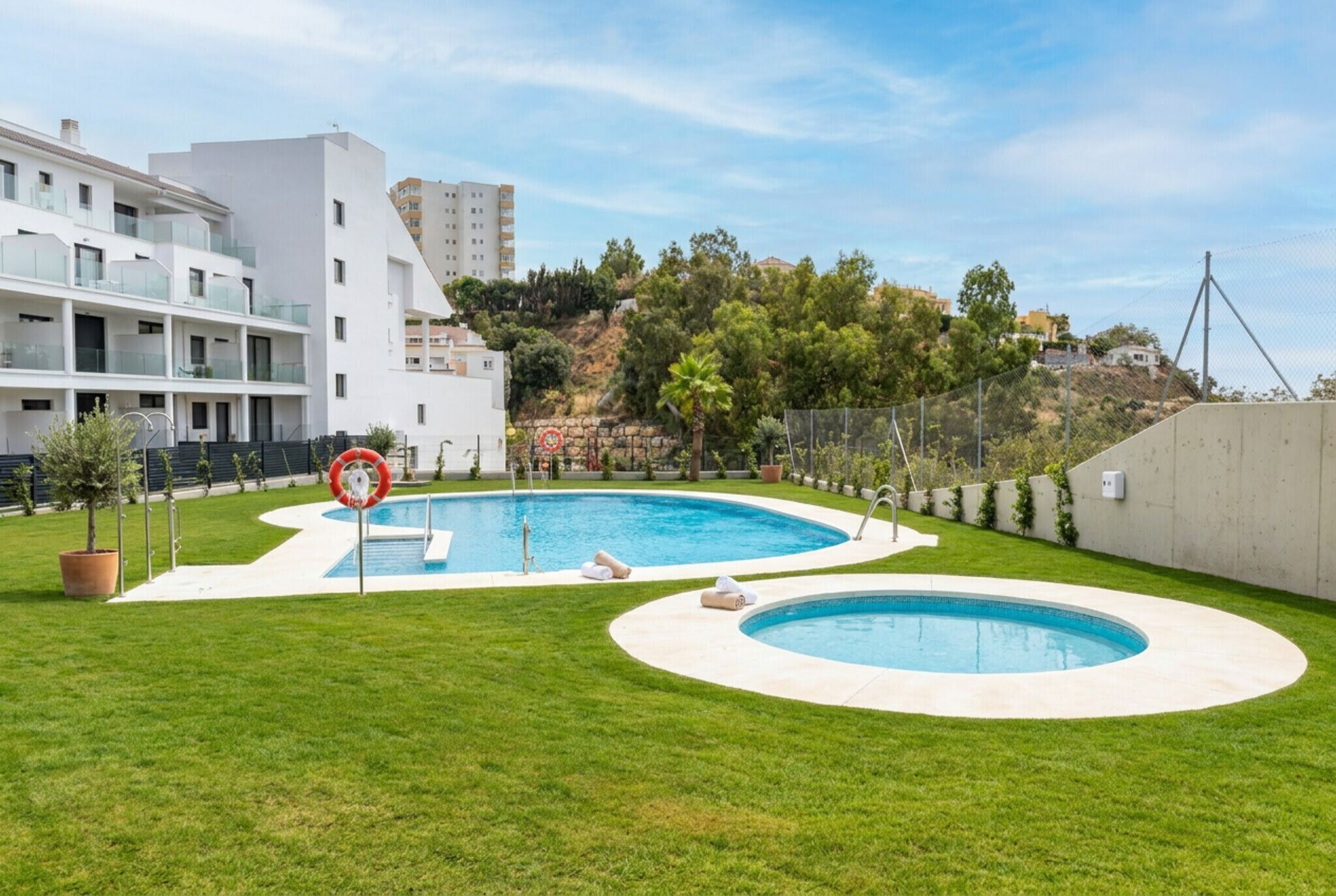 A swimming pool with a lifebuoy, surrounded by a well-maintained lawn, and adjacent to a modern building with balconies.
