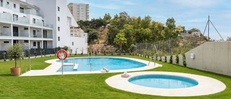 Une piscine équipée d’une bouée de sauvetage, entourée d’une pelouse bien entretenue, et jouxtant un bâtiment moderne doté de balcons.