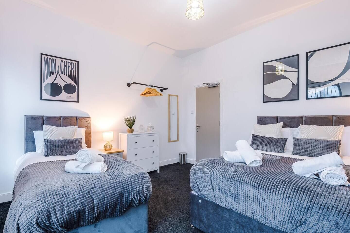 Et moderne hotelværelse med to senge, en kommode, et spejl og kunst på væggene.