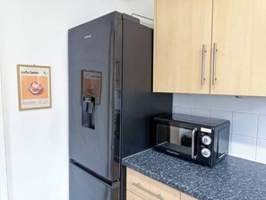 A kitchen with a stainless steel refrigerator, a black toaster, and wooden cabinets. - 3 BR House | Sleeps 7 | Free Parking | Fast Wi-Fi (Greater Manchester)