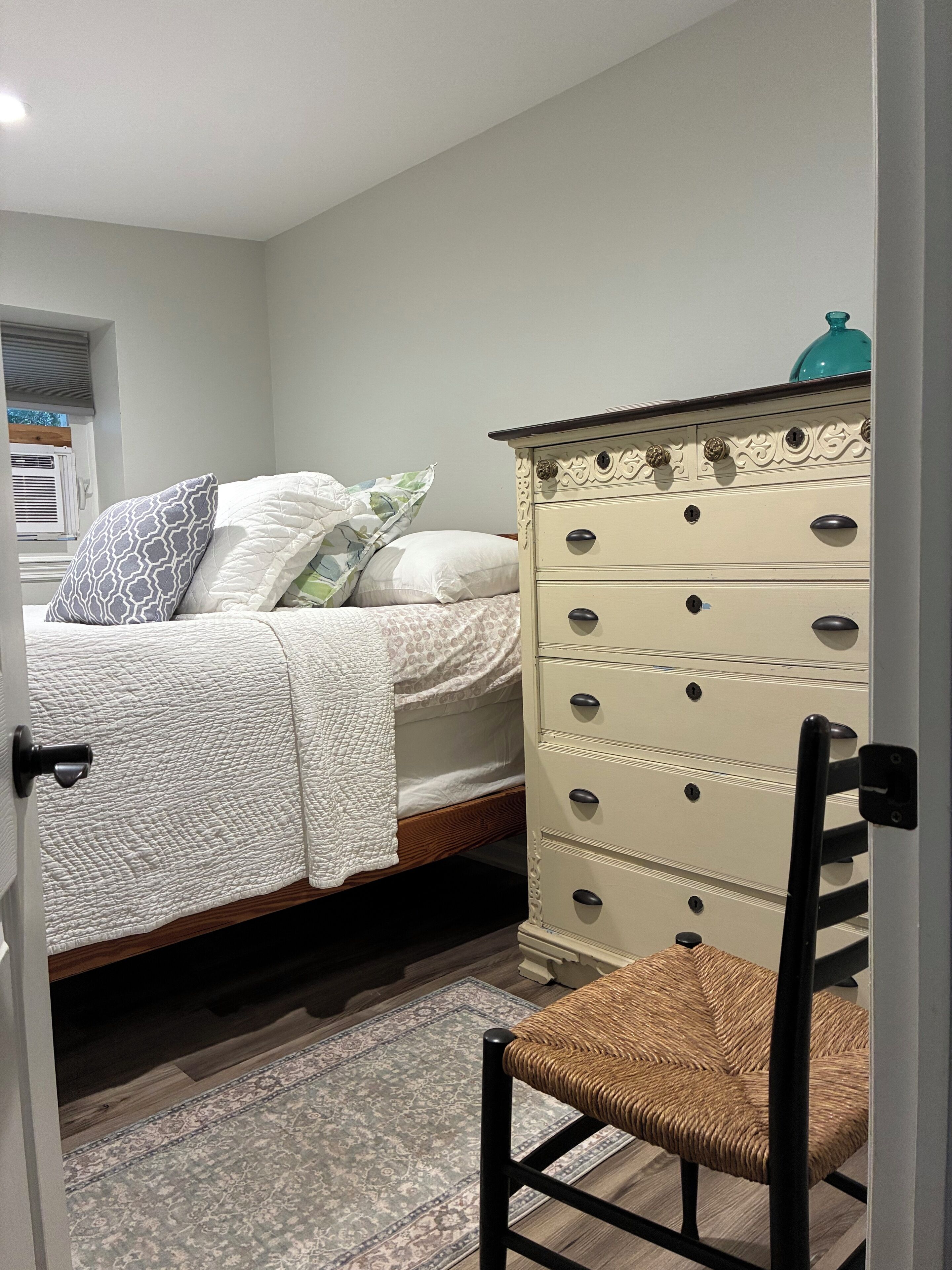 A bedroom with a bed, a dresser, a chair, and a patterned rug.