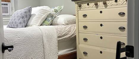 A bedroom with a bed, a dresser, a chair, and a patterned rug.