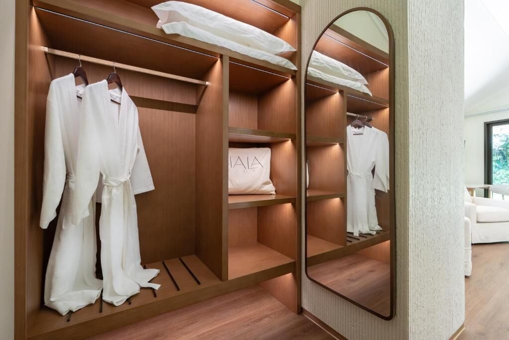 Un vestidor con estantes de madera, un espejo y batas colgadas.