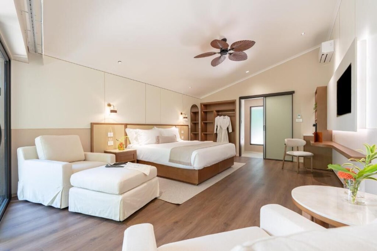 A modern hotel room with a large bed, a sofa, a dining table, and a ceiling fan.