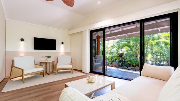 A modern living room with a sofa, chairs, a coffee table, and a TV mounted on the wall. - NALA Resort (Mission Beach)