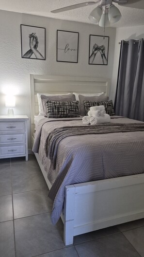 Ein ordentlich gemachtes Bett mit einem gemusterten Überwurf, ein Nachttisch mit einer Lampe und drei gerahmte Bilder an der Wand.