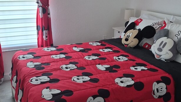 A bedroom with a bed covered in a Mickey Mouse themed blanket, a ceiling fan, and wall decorations including framed pictures and Mickey Mouse silhouettes. - Comfortable Home Near Disney ,Private Entrance & Free Parking (Davenport)