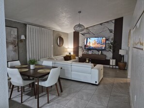 Ein modernes Wohnzimmer mit Sofa, Esstisch und Fernseher.