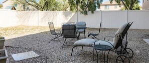 An outdoor patio with a table and chairs, surrounded by a white fence and trees.