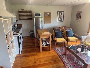 A compact kitchen with a microwave, refrigerator, and wooden dining table with chairs. - Cosy cottage with beautiful mountain view. Close to town and Carrot Park. (Ohakune)