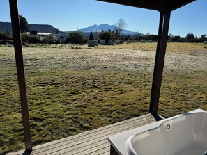 A wooden deck with a hot tub, a grassy field, and a mountain in the background. - Cosy cottage with beautiful mountain view. Close to town and Carrot Park. (Ohakune)