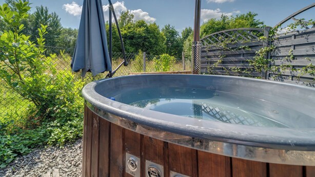 A wooden hot tub with a glass top, surrounded by greenery and a wooden fence. - Superior by Interhome (Leśna)