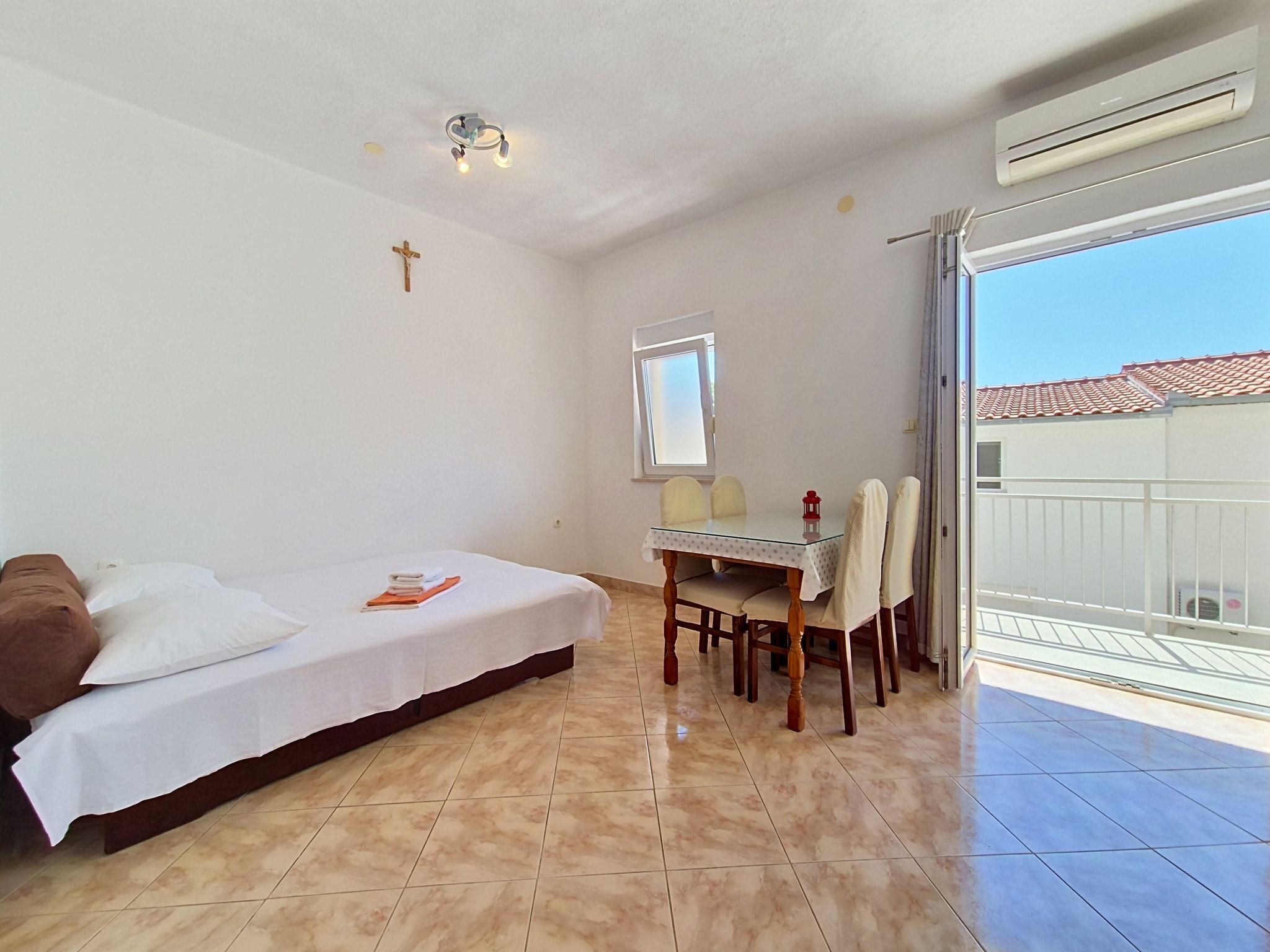 Une chambre à coucher avec un lit, une table à manger avec des chaises, une croix accrochée au mur et un appareil de climatisation.