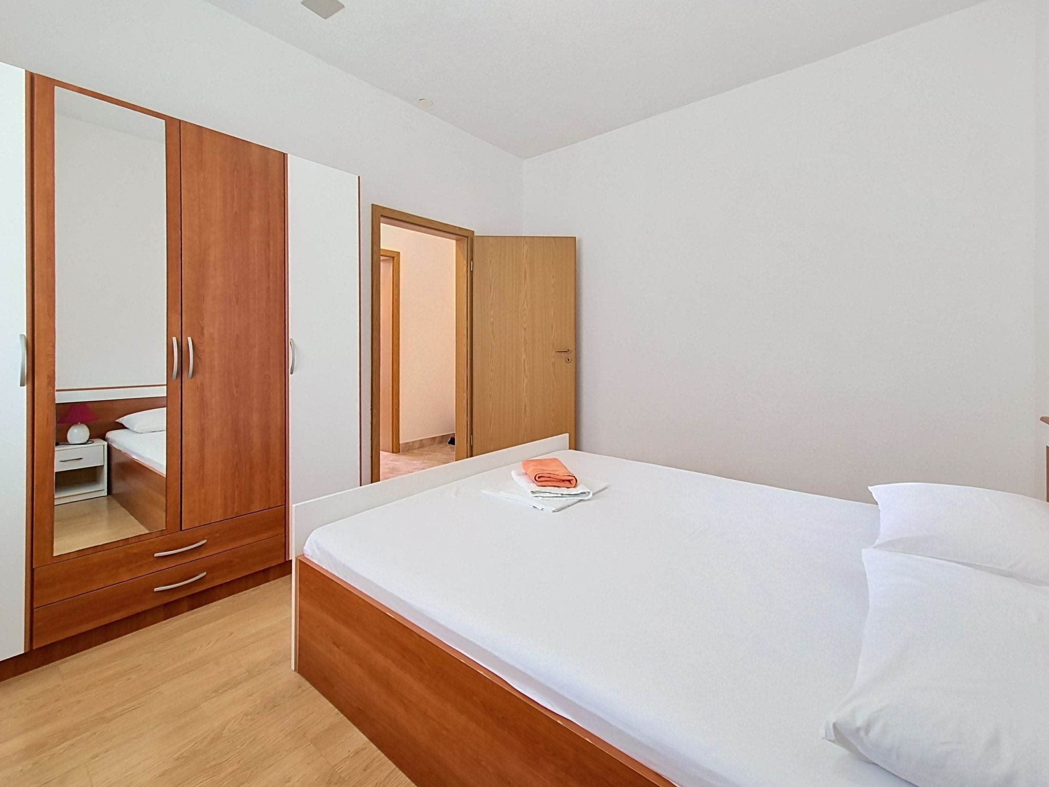 A bedroom with a wooden wardrobe, a bed with white linens, and a mirror.