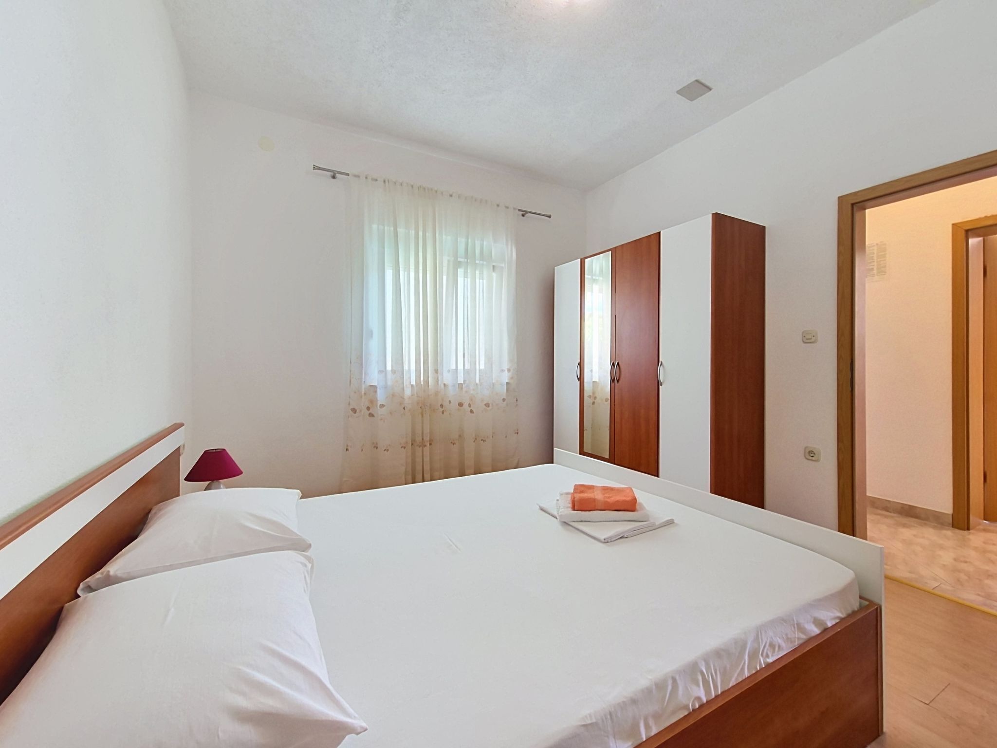 A bedroom with a bed, a wardrobe, a window with curtains, and a lamp.