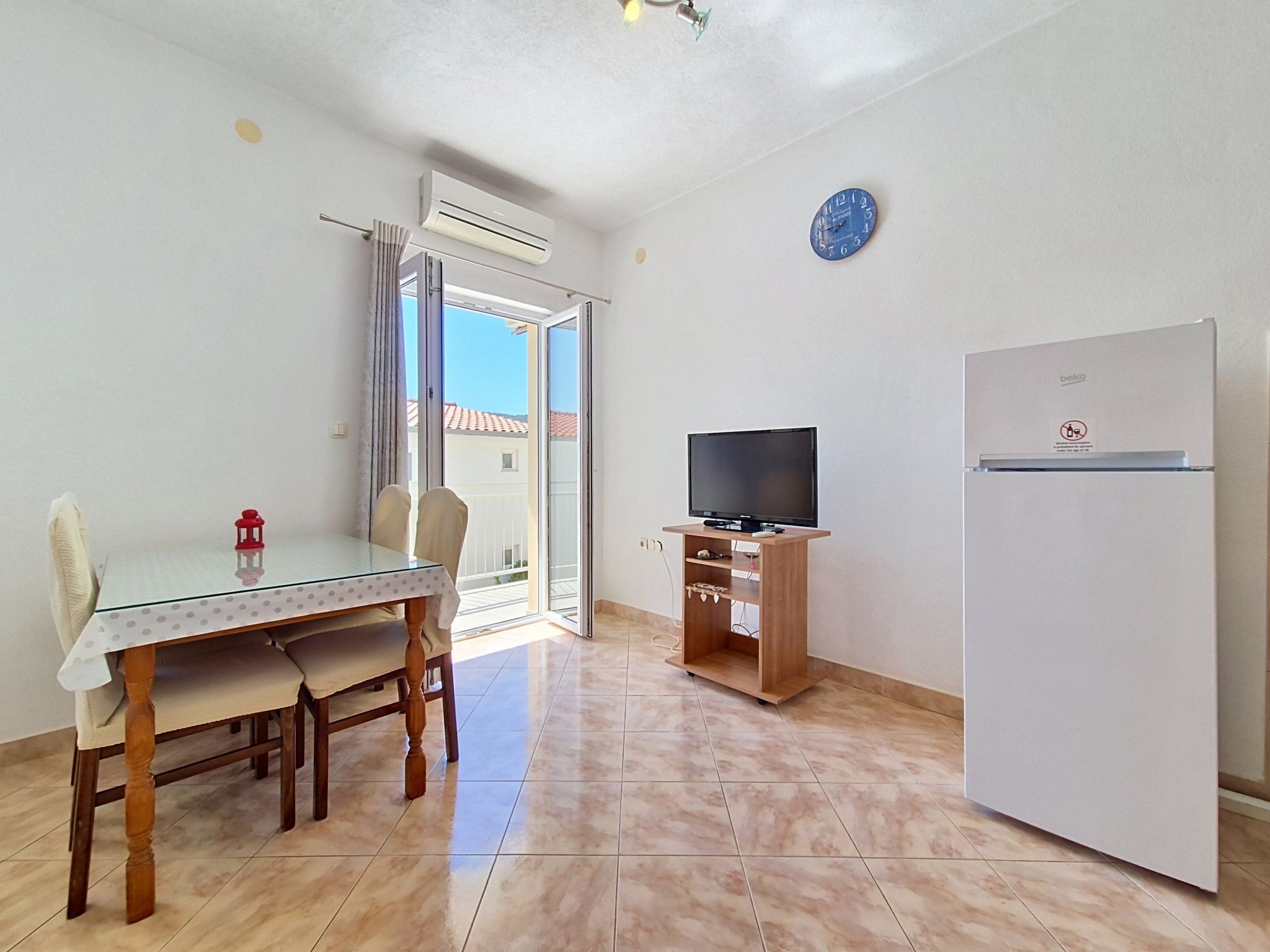 A room with a dining table, chairs, a television, and a refrigerator.