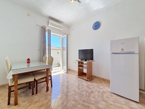 Ein Zimmer mit Esstisch, Stühlen, Fernseher und Kühlschrank.