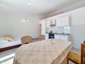 A compact kitchen with white cabinets, a dining table with a patterned tablecloth, and a bed with a patterned pillow. - Vukelja by Interhome (Marina)