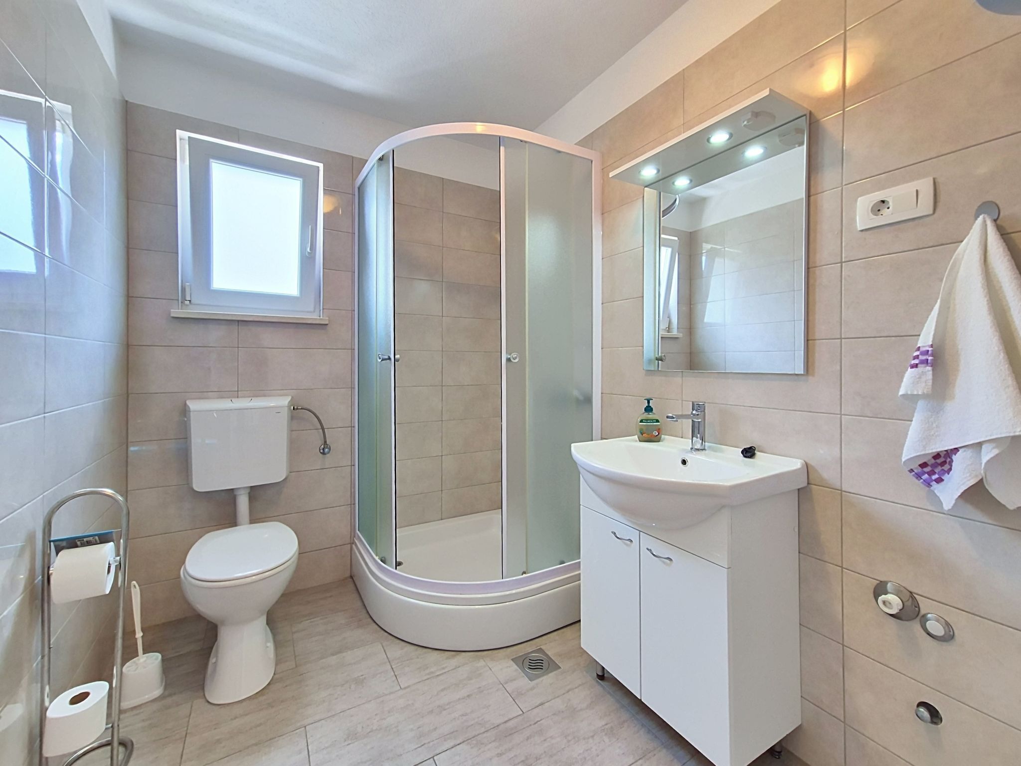 Ein modernes Badezimmer mit Toilette, Duschkabine, Waschbecken und Spiegel.