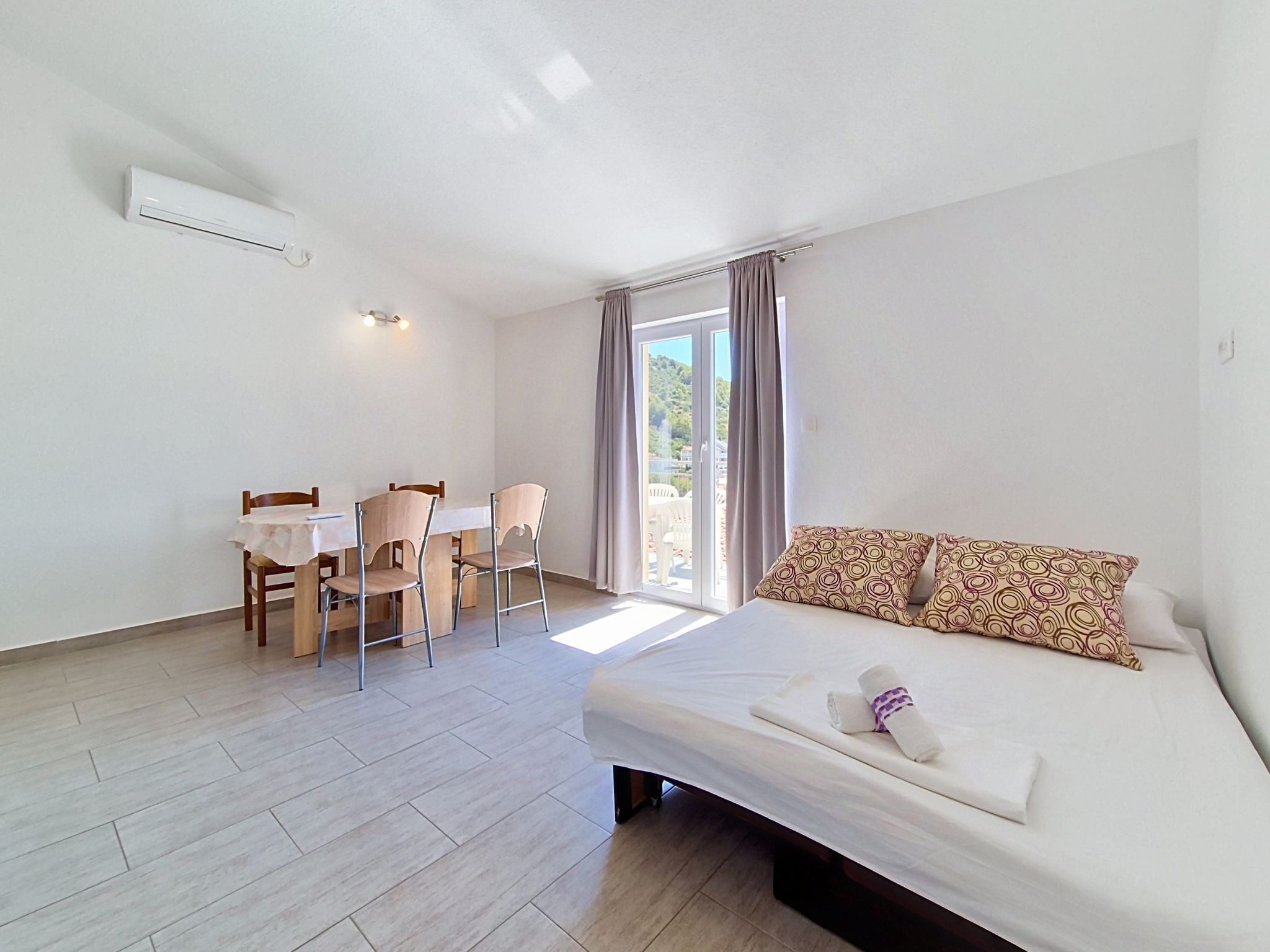 A hotel room with a bed, a desk with chairs, and a window with curtains.