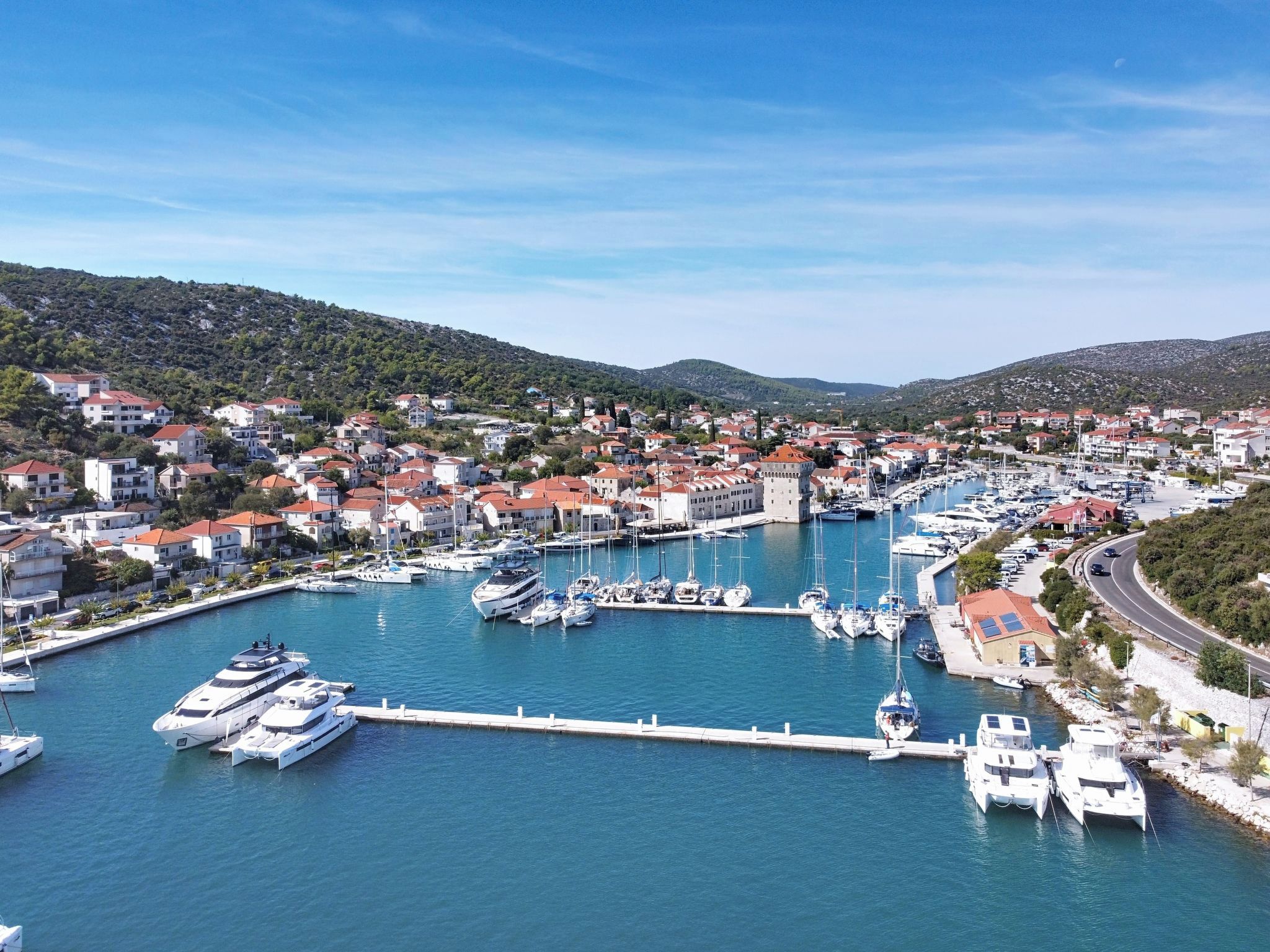 A marina with boats docked, surrounded by residential buildings and hills in the background.