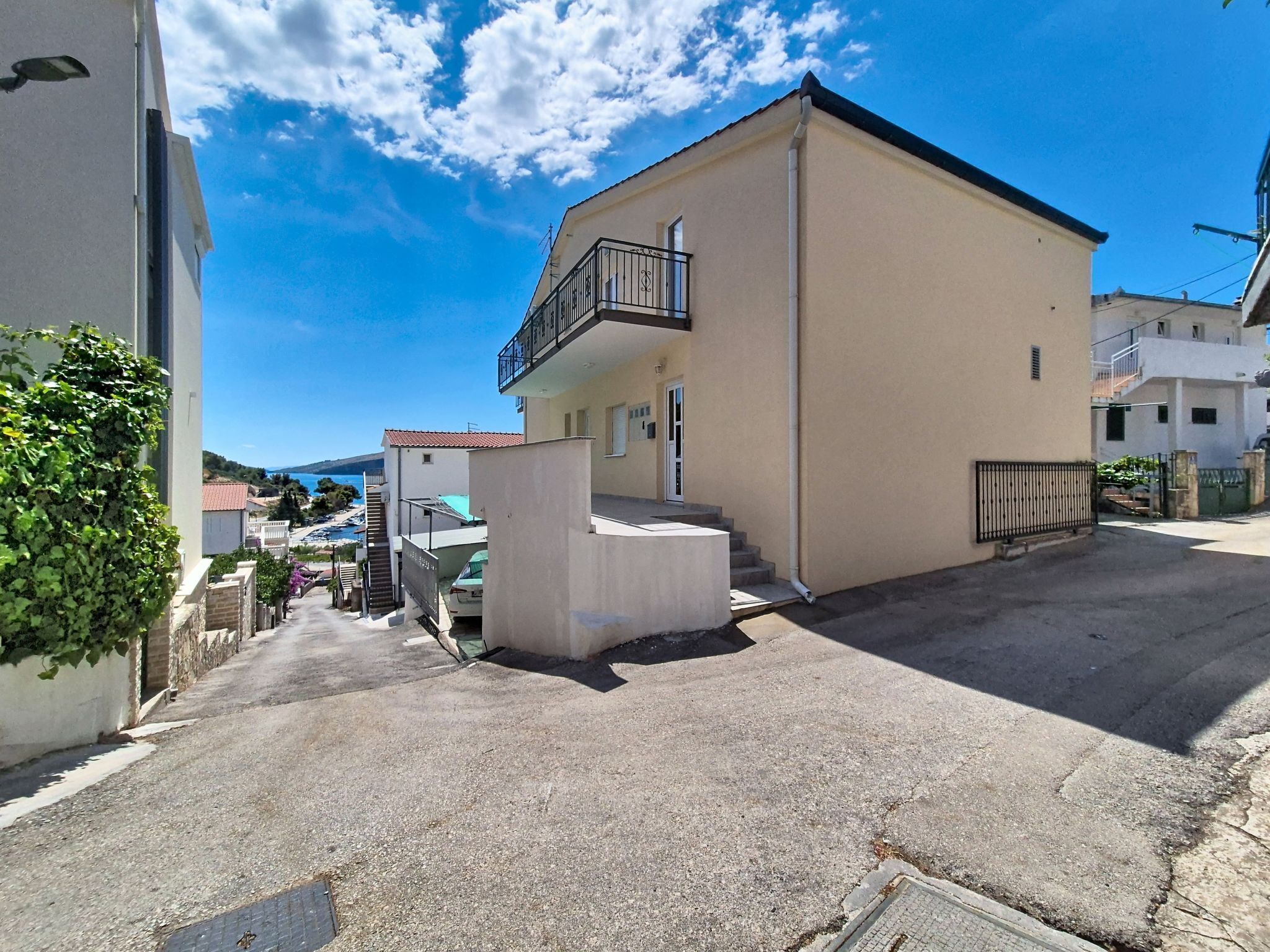 Une rue résidentielle bordée d’un immeuble à deux étages, doté d’un balcon et d’une petite structure en béton à l’avant.