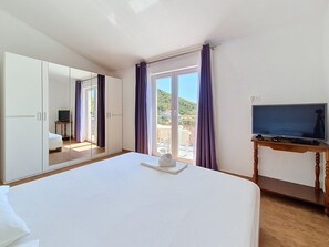 A hotel room with a large bed, a television on a wooden table, and a view of a balcony with purple curtains. - Vukelja by Interhome (Marina)