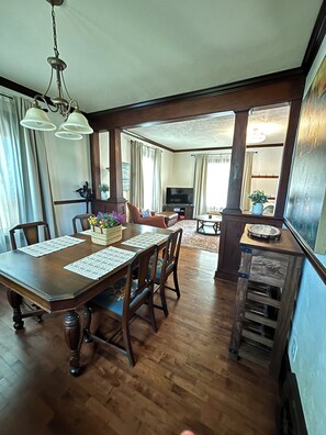 A dining area with a wooden table and chairs, a television in the background, and a staircase leading to another room.