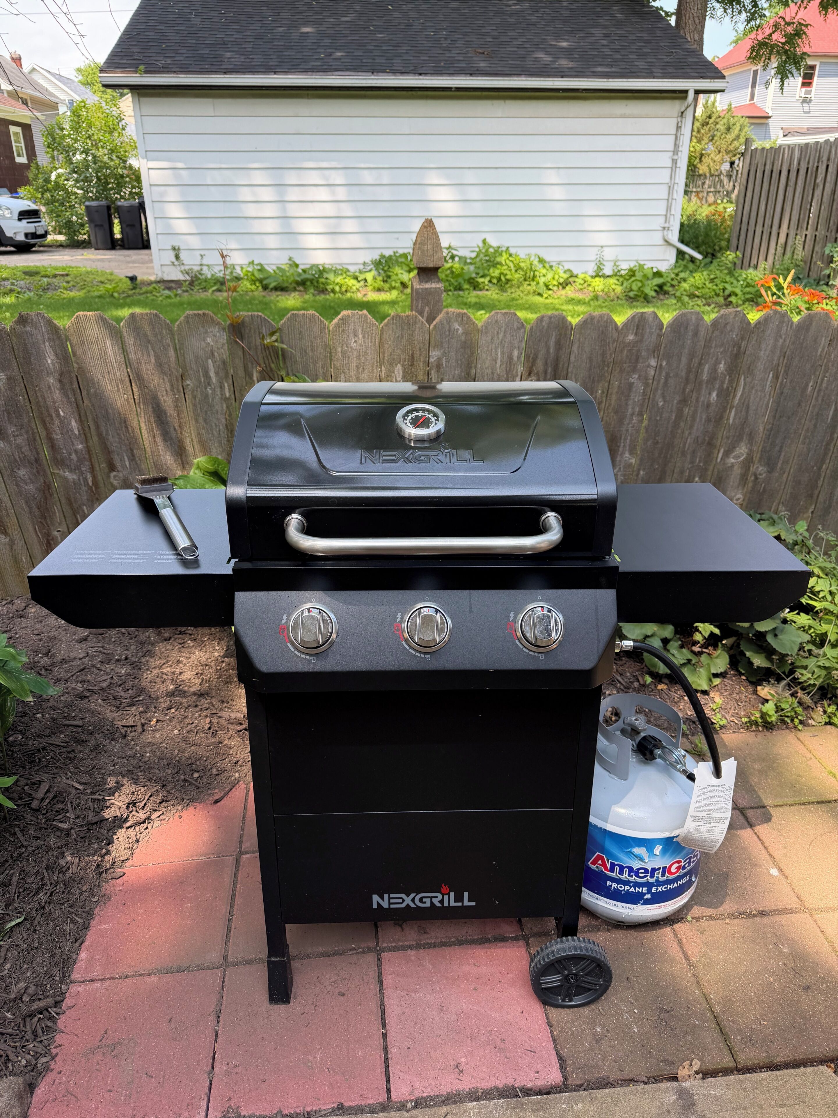 A black NexGrill barbecue grill with three control knobs, a propane tank, and a brush.