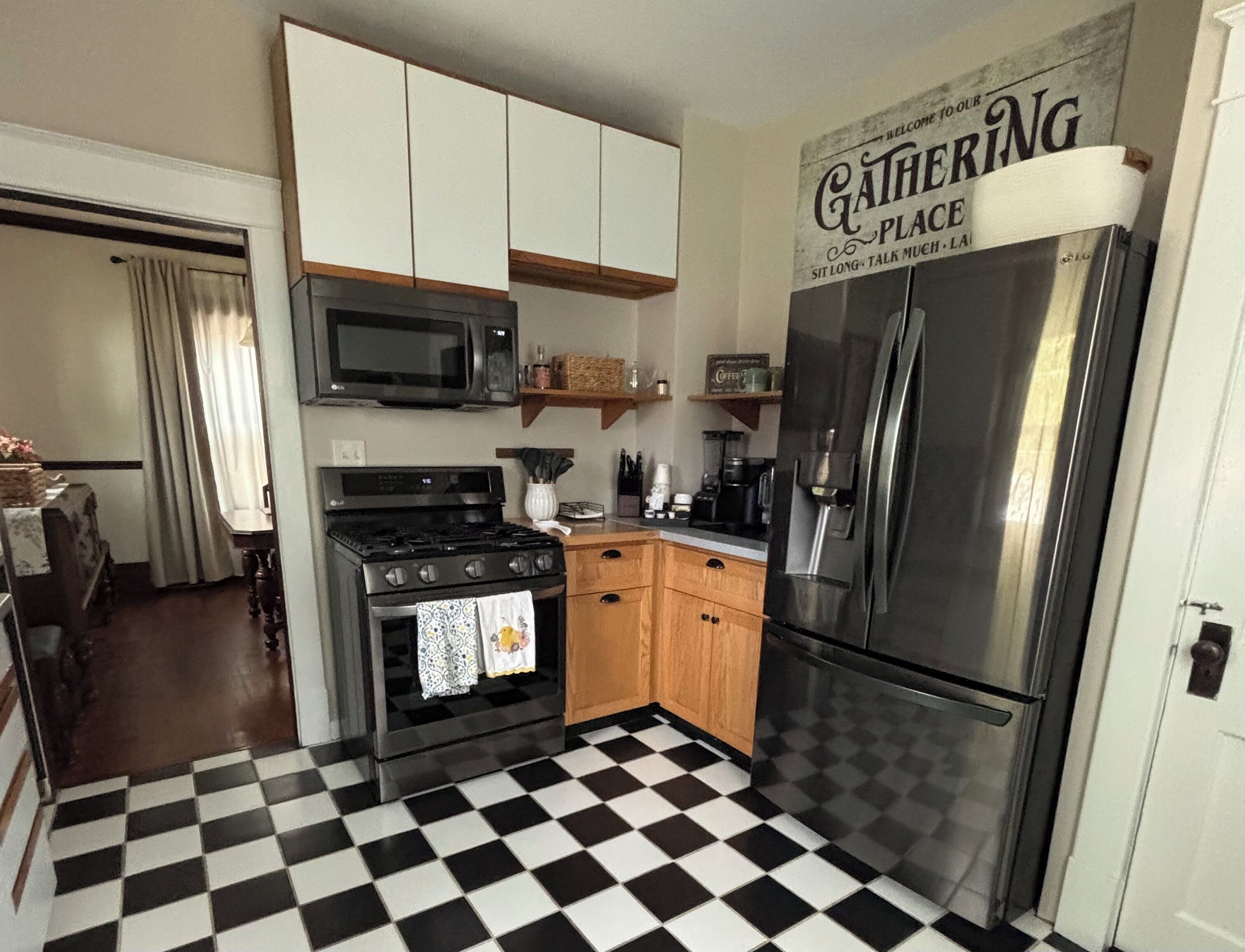 A kitchen with a black and white checkered floor, a stainless steel refrigerator, an LG stove, and a microwave.