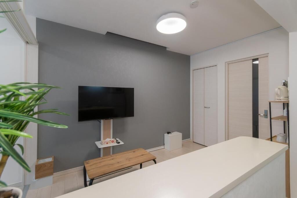 A modern bathroom with a flat-screen TV mounted on the wall, a bench, and a white countertop.