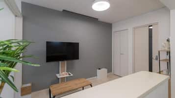 A modern bathroom with a flat-screen TV mounted on the wall, a bench, and a white countertop.