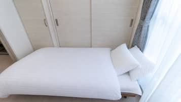 A single-bed room with a wooden wardrobe, a window with curtains, and a light-colored floor.
