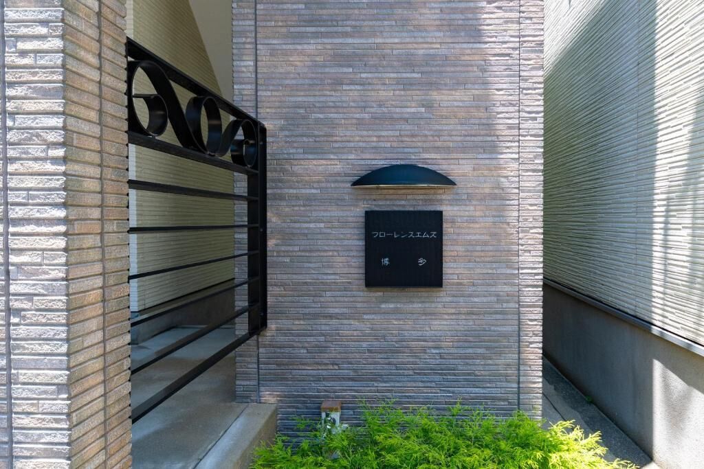 A modern building facade with a stone-textured wall, a metal gate, and a black sign with white text.