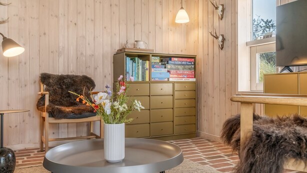 Una habitación acogedora con paredes de madera, una estantería, una mesa redonda con un florero y un sillón de pelo, además de un televisor.